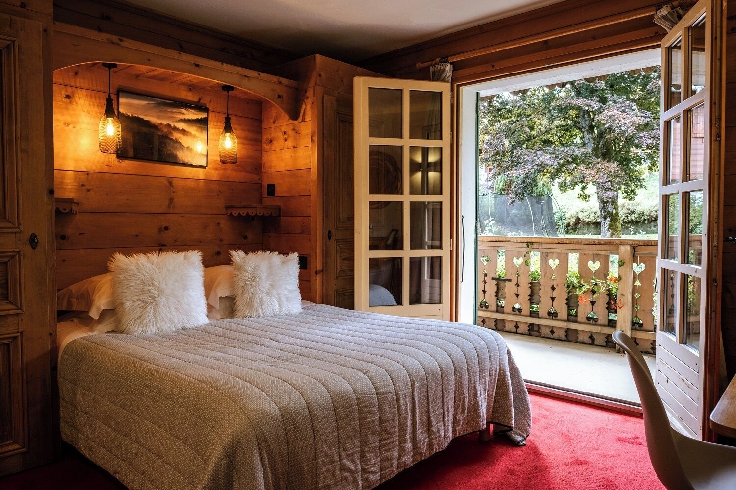 A cozy wooden room with a bed, a balcony with a wooden railing, and a view of trees.