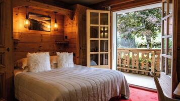 A cozy wooden room with a bed, a balcony with a wooden railing, and a view of trees.