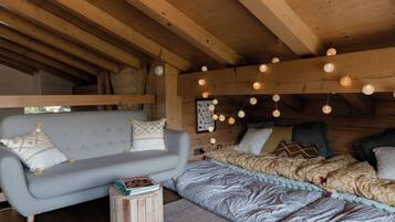 Interior acogedor de una cabaña con sofá, cama con ropa de cama estampada y techo de madera con luces colgantes.