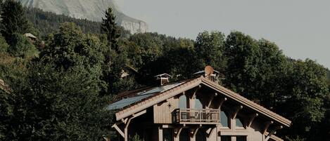 Une cabane en bois dotée d’un balcon, entourée d’une forêt dense et avec une montagne en arrière-plan.