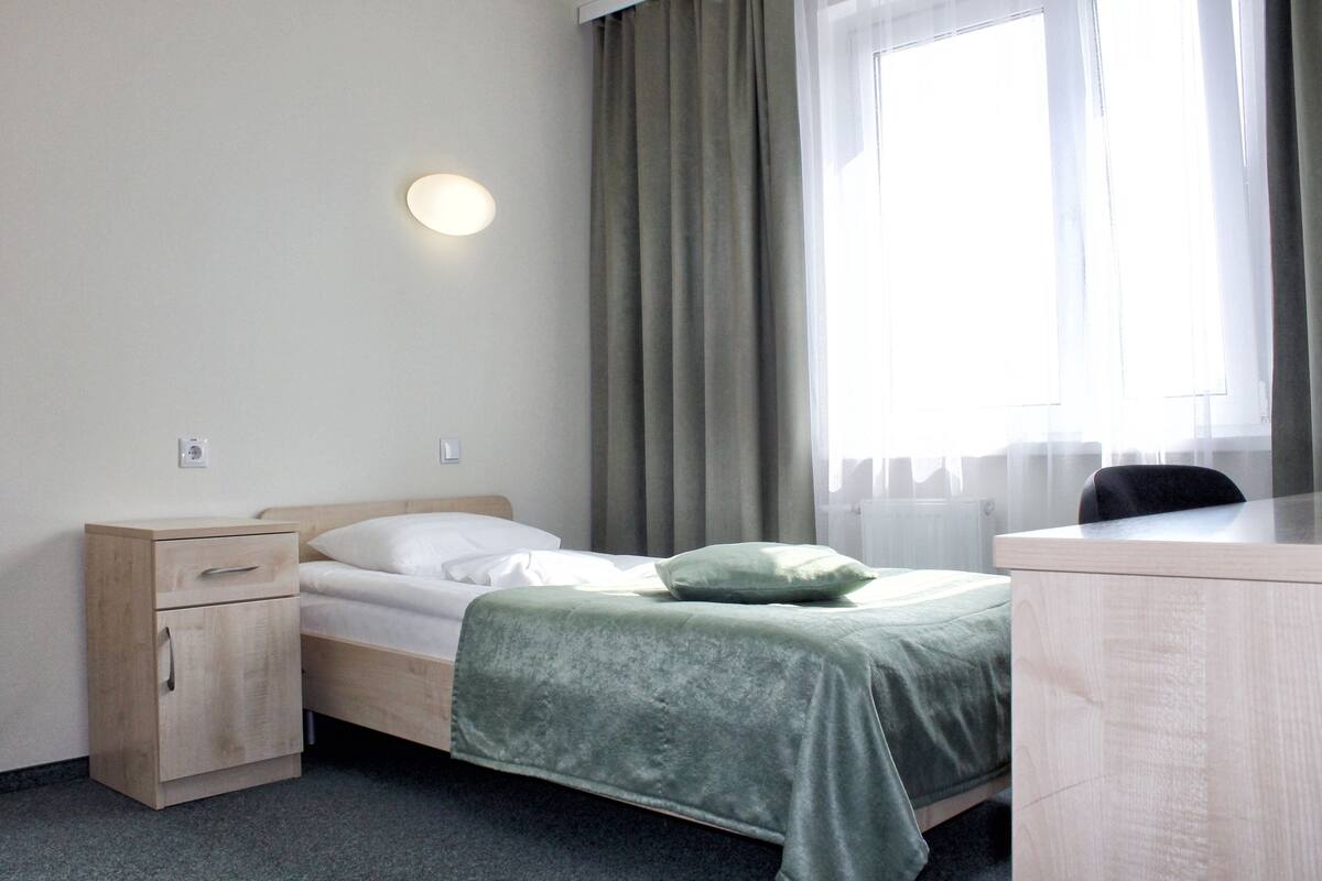 A hotel room with a bed, a desk, a nightstand, and a window with curtains.
