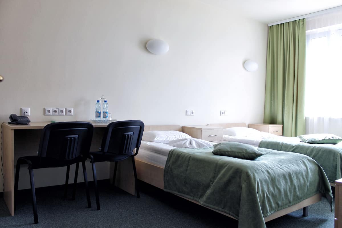 A hotel room with two beds, a desk with chairs, a telephone, and a water dispenser.