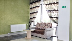 A waiting area with a sofa, a small table, a radiator, and a window with curtains. - Sport Time Hotel (Minsk)