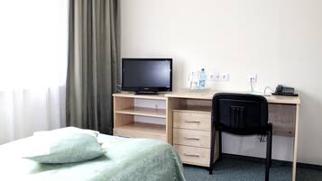 A hotel room with a bed, a desk with a computer, a chair, and a window with curtains.