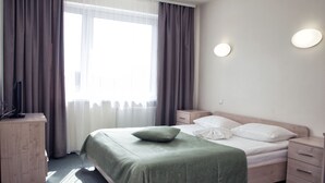 A hotel room with a bed, bedside tables, a dresser, and a window with curtains. - Sport Time Hotel (Minsk)