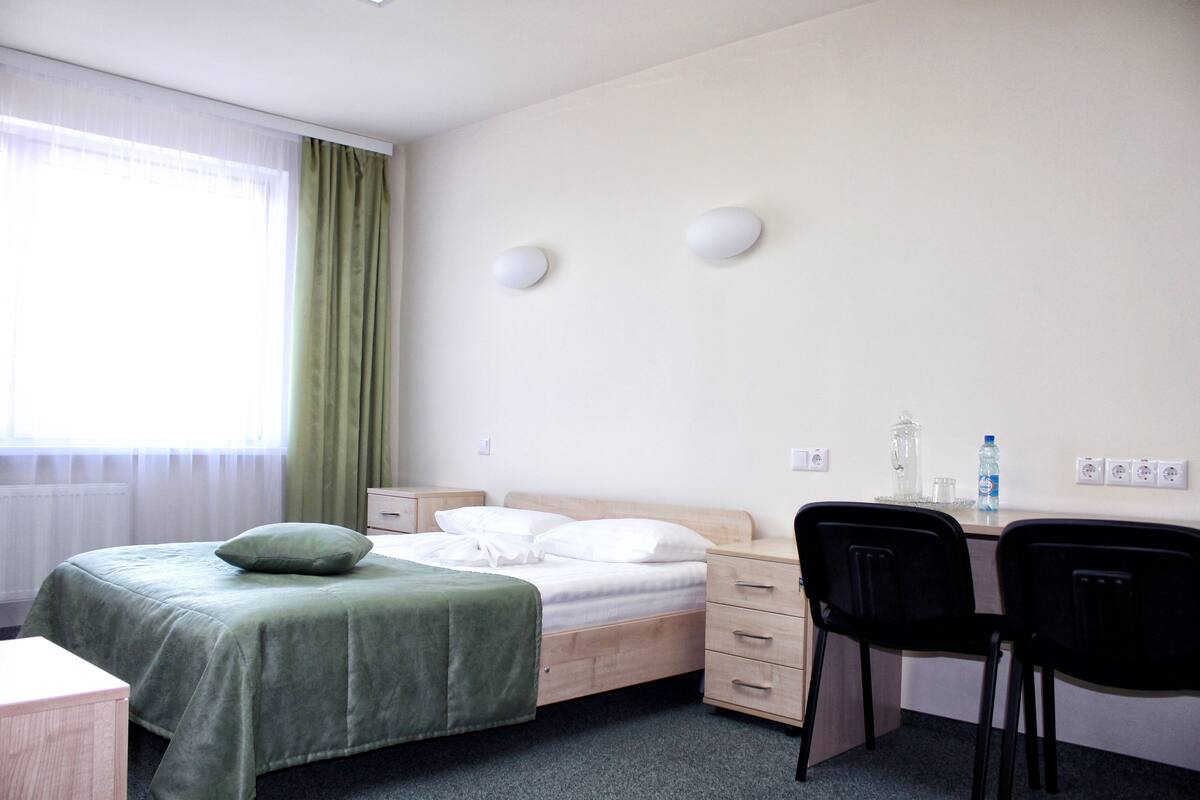 A hotel room with a bed, a desk with two chairs, a nightstand, and a window with curtains.