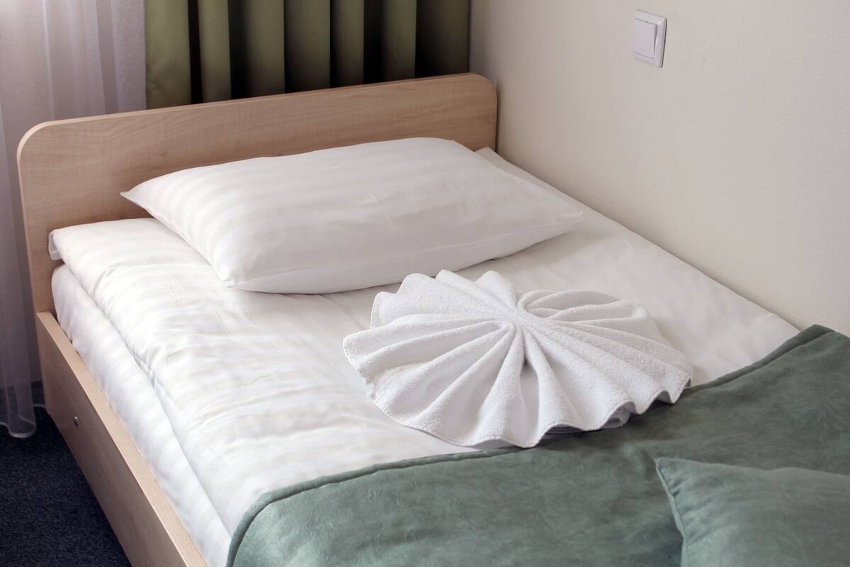 A neatly made bed with white linens and a green throw blanket.