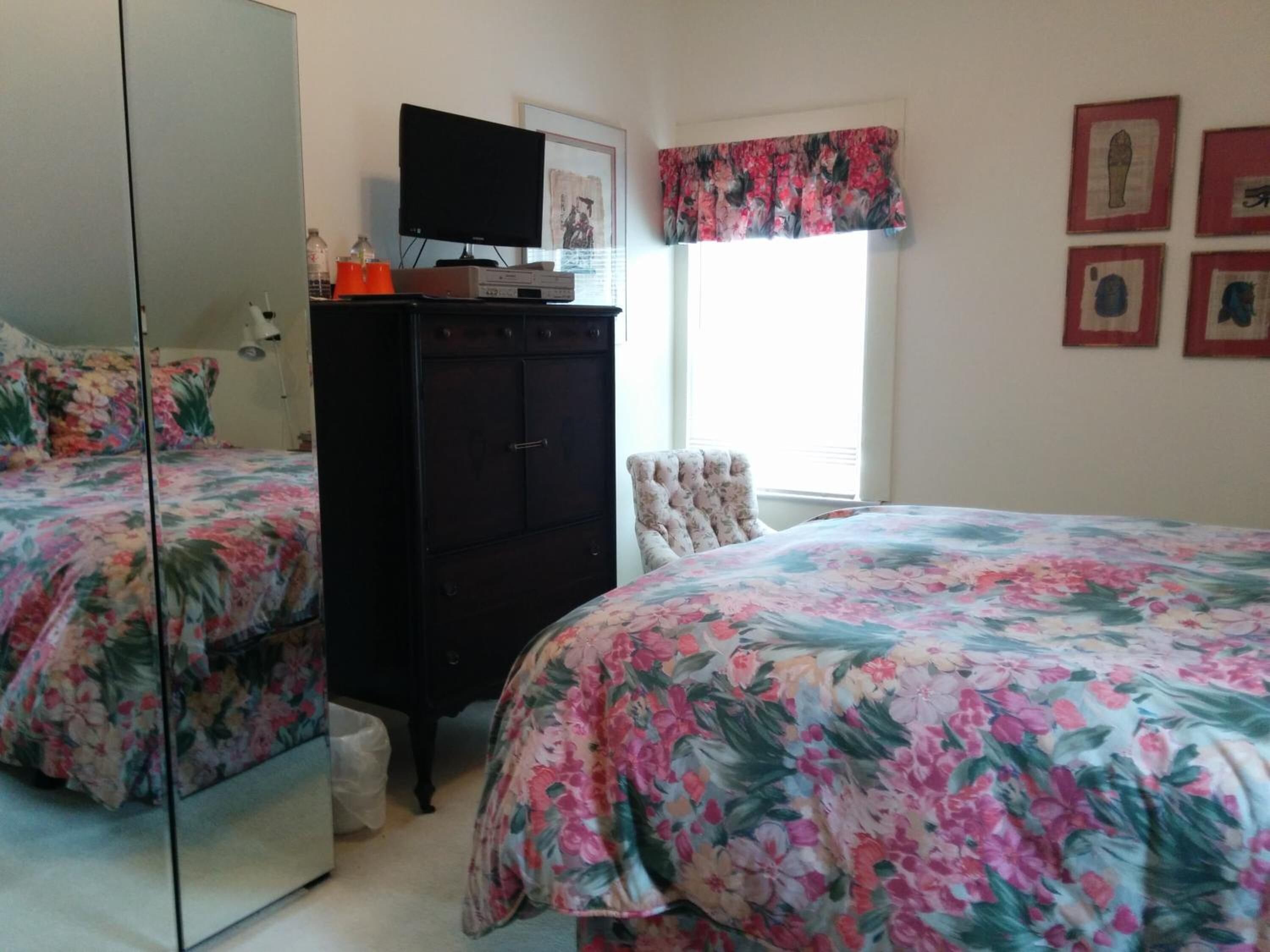 Un dormitorio con dos camas, un aparador, un espejo y una ventana con cortinas.