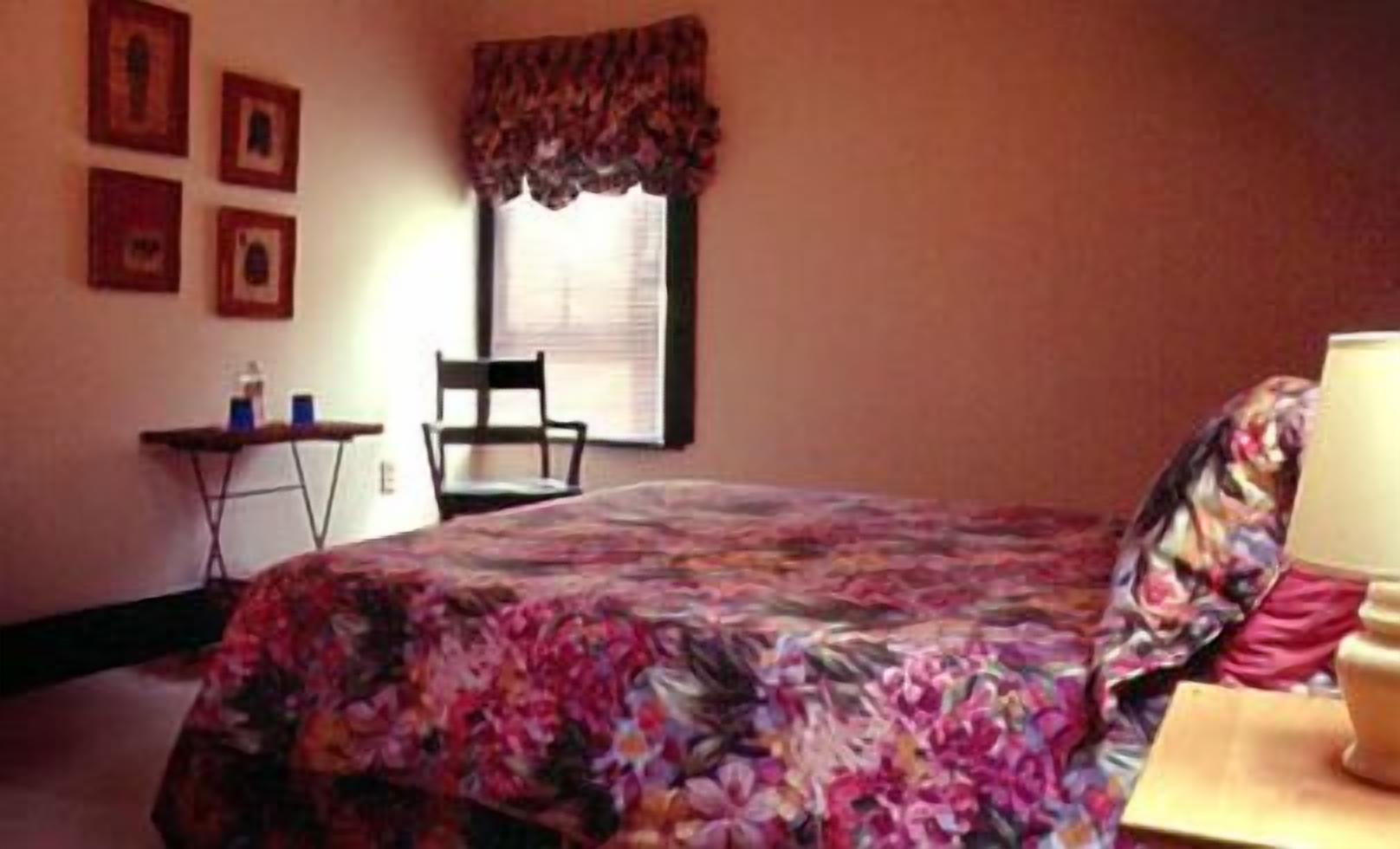 A bedroom with a bed, a chair, a small table, and a window with curtains.