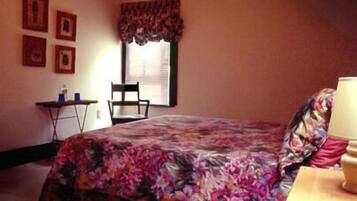A bedroom with a bed, a chair, a small table, and a window with curtains.