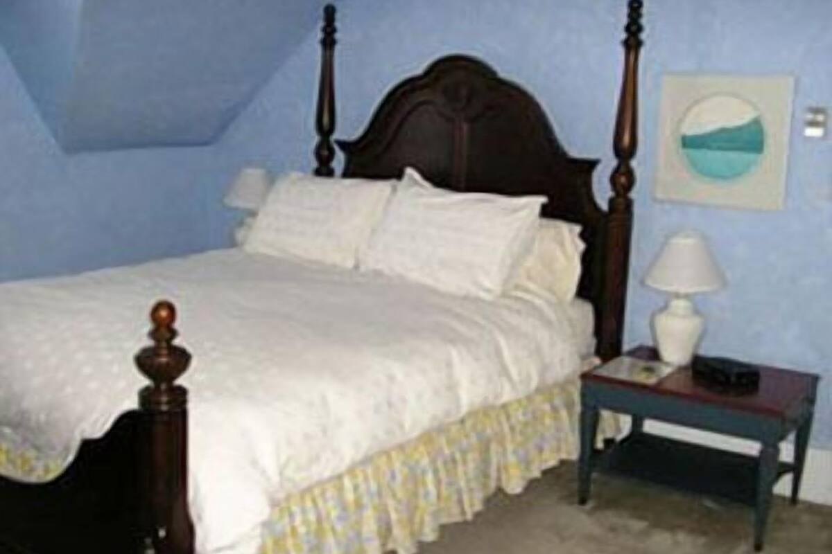Une chambre à coucher avec un lit à baldaquin, du linge de lit blanc, une table de chevet avec une lampe et un tableau accroché au mur.
