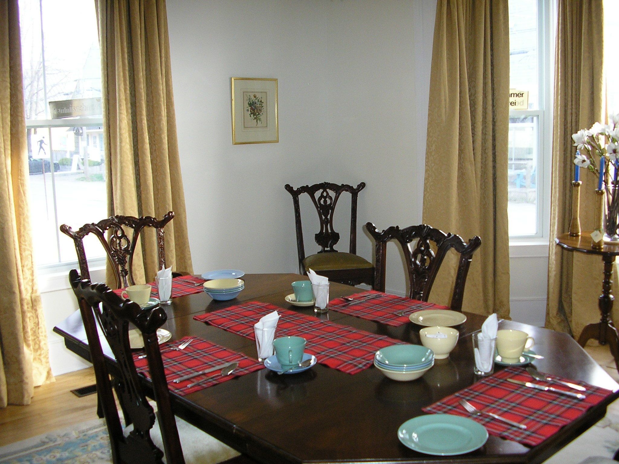 Une salle à manger avec une table en bois dressée pour quatre personnes, des sets de table à carreaux et des chaises assorties.