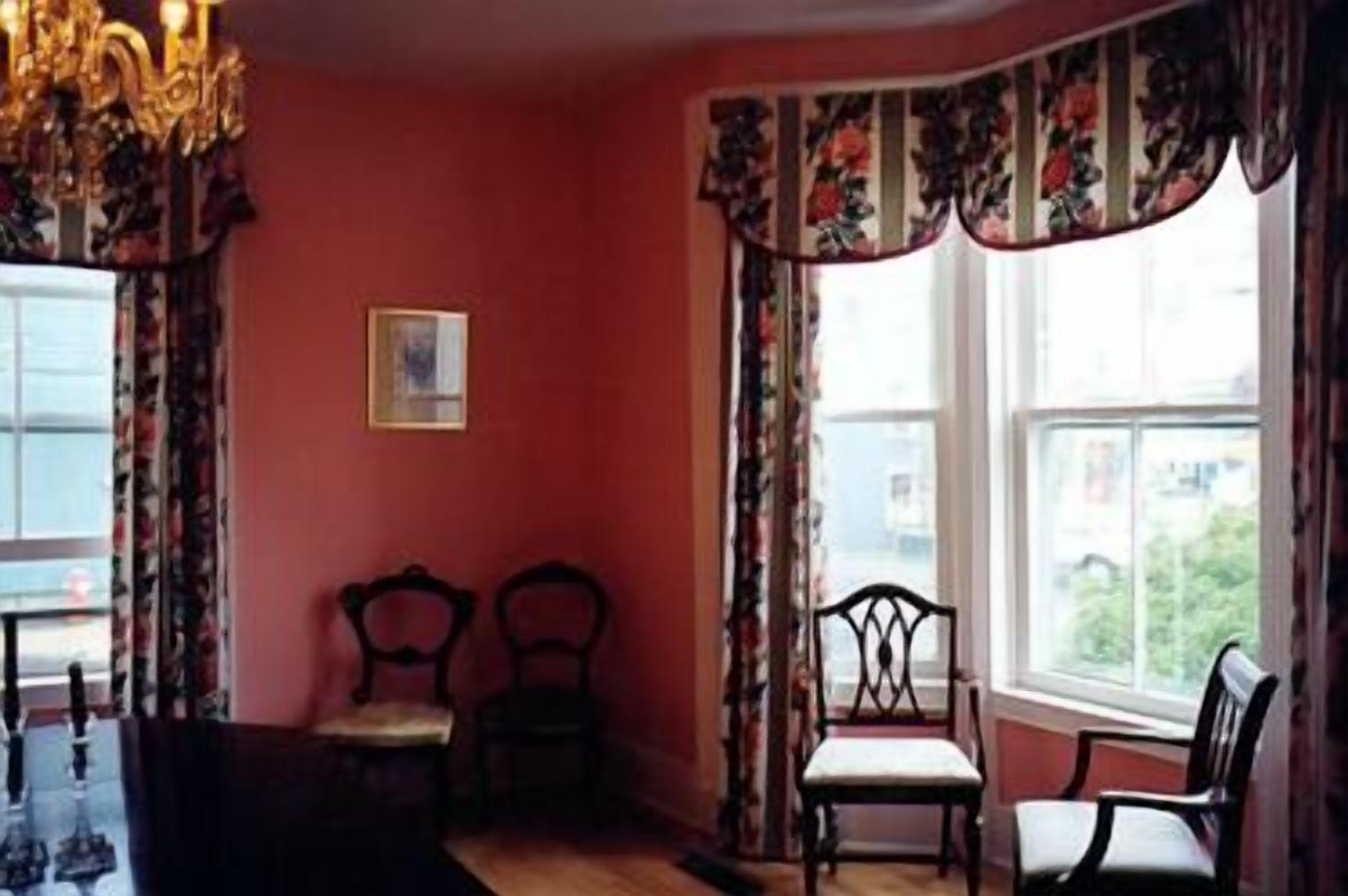 Una habitación con dos sillas, una araña y un ventanal con cortinas florales.