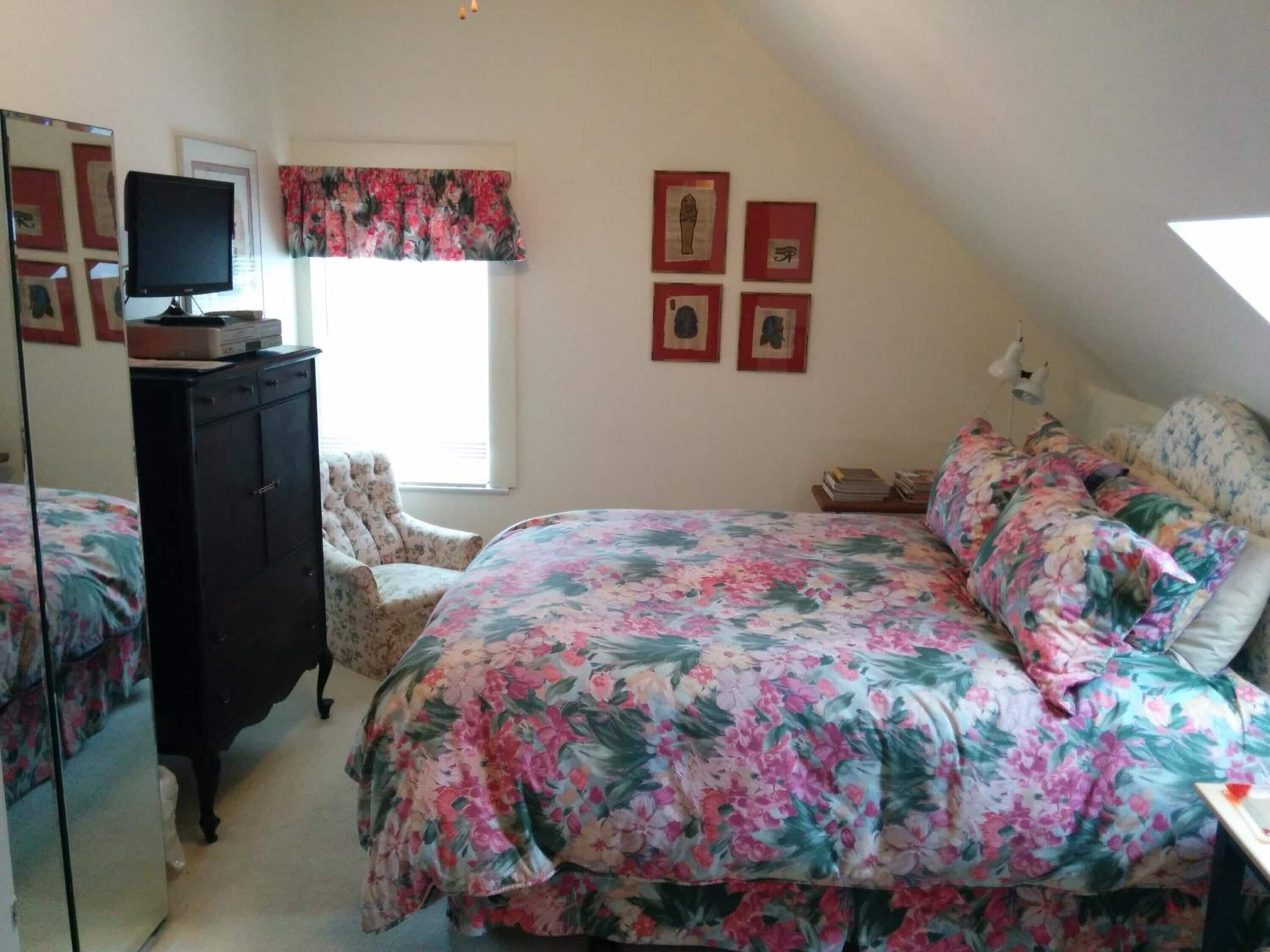 Quarto com cama, penteadeira, cadeira e televisão sobre a penteadeira.
