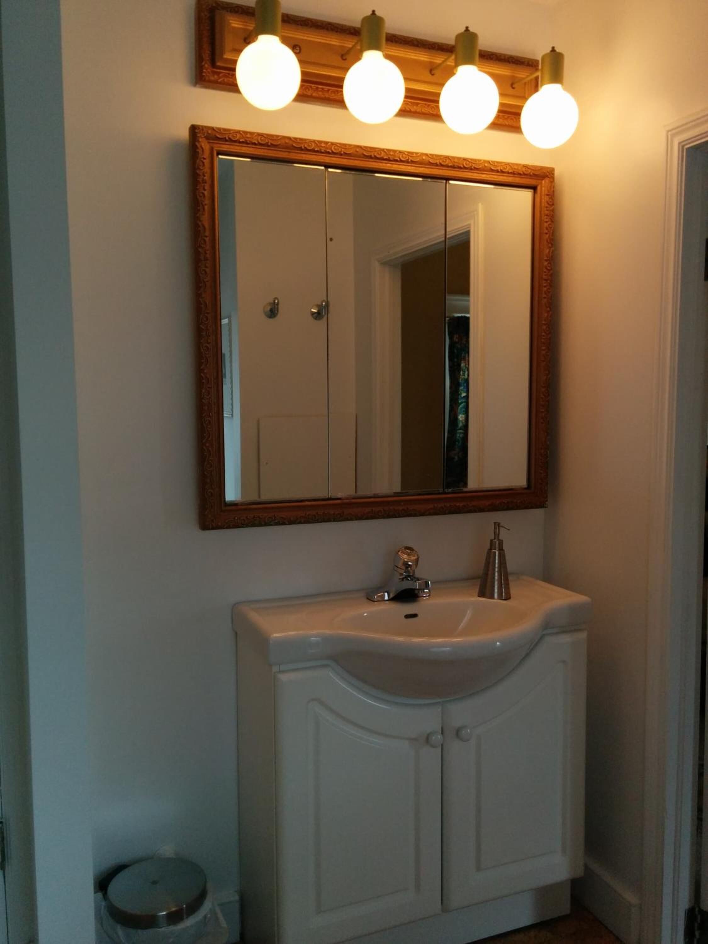 Une salle de bain avec un meuble-lavabo blanc, un miroir avec un cadre en bois et trois appliques murales rondes.