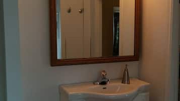 Une salle de bain avec un meuble-lavabo blanc, un miroir avec un cadre en bois et trois appliques murales rondes.