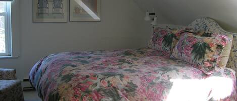 A bedroom with a floral bedspread, a nightstand with a lamp, and two framed pictures on the wall.