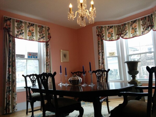 A dining room with a large table, chairs, a chandelier, and floral curtains. - Fairmont House Bed & Breakfast (Mahone Bay)