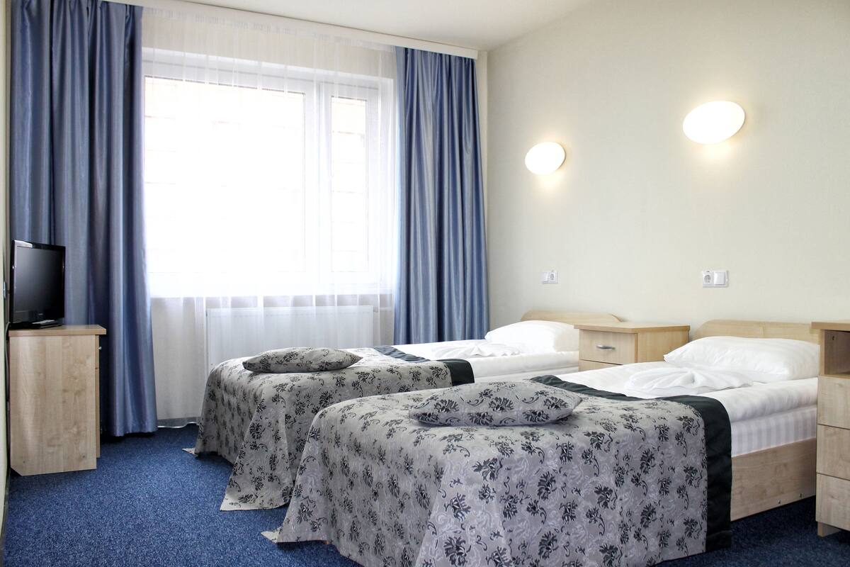 A hotel room with two beds, a television on a wooden cabinet, and a window with curtains.