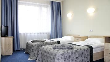 A hotel room with two beds, a television on a wooden cabinet, and a window with curtains.