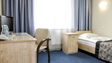Ein Hotelzimmer mit Schreibtisch, Stuhl, Bett, Nachttisch und einem Fenster mit Vorhängen.