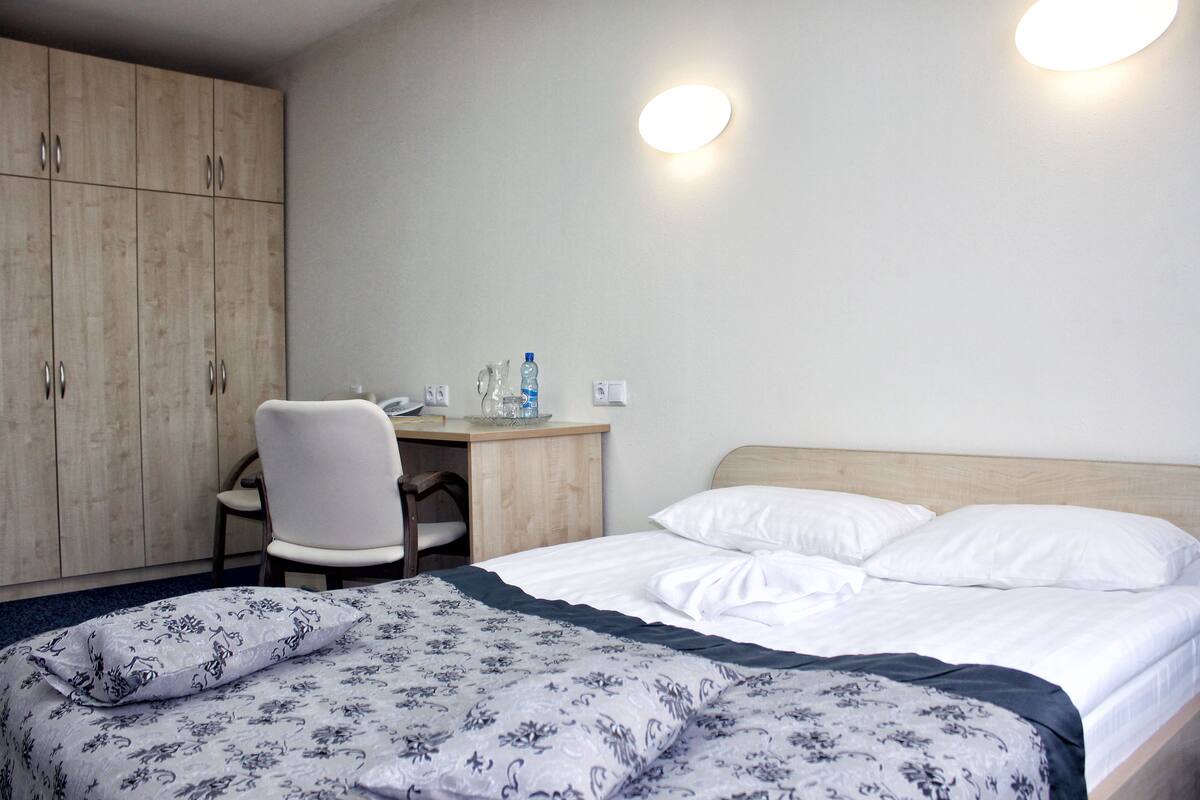 A hotel room with a bed, a desk, a chair, and a wardrobe.