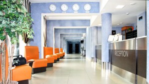 Un espace d’accueil d’hôtel comprenant un comptoir de réception, un coin salon et des horloges murales.