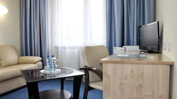 Habitación de hotel con sofá, una mesita con un tray de botellas de agua, una silla, televisor y una mesita de noche de madera.