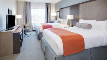A hotel room with two beds, a desk with a TV, and a window with curtains.