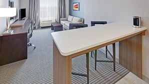 Habitación de hotel con escritorio, sofá, televisión, cafetera y ventana con cortinas.