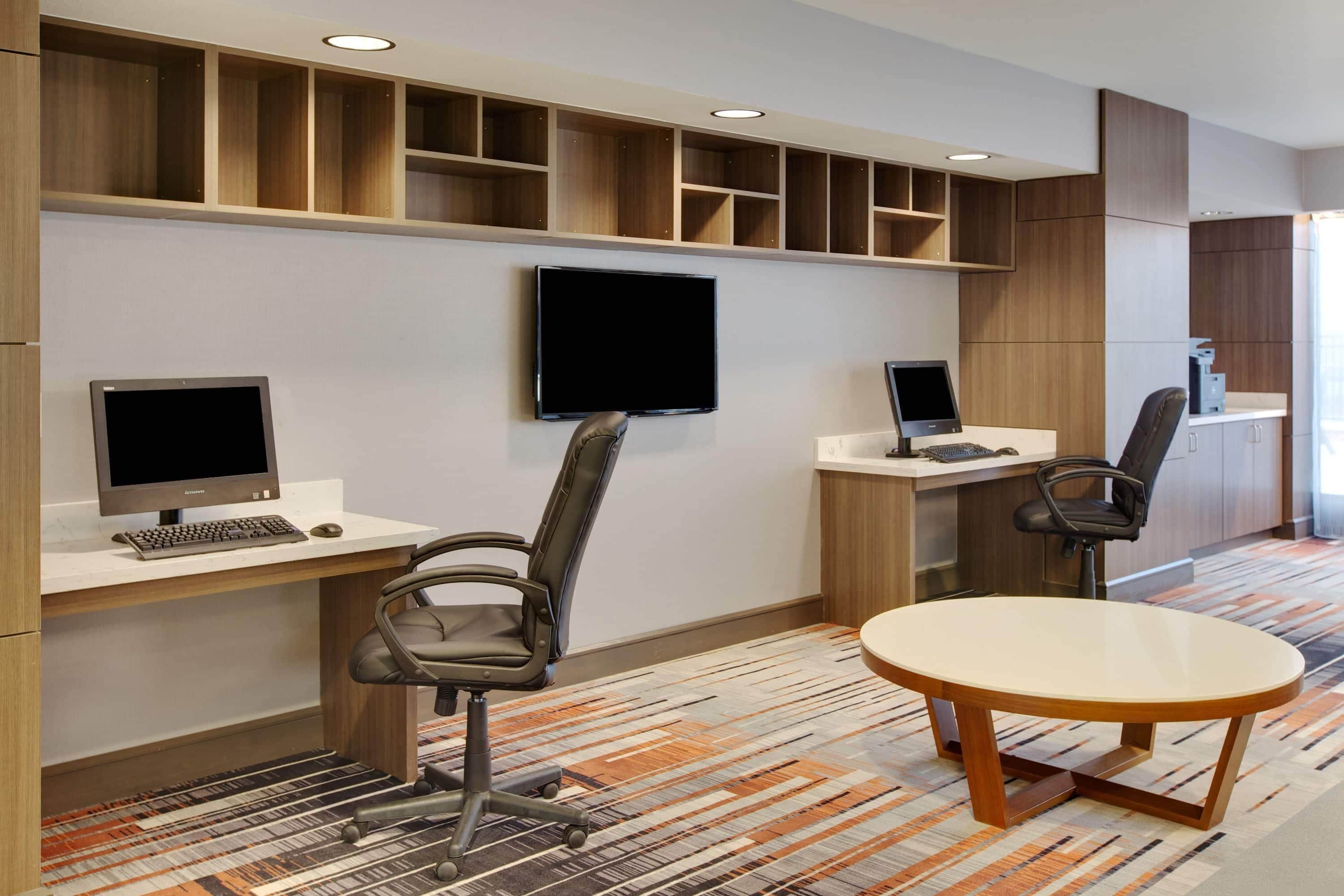 A modern office space with two desks, chairs, a round table, and built-in shelving.