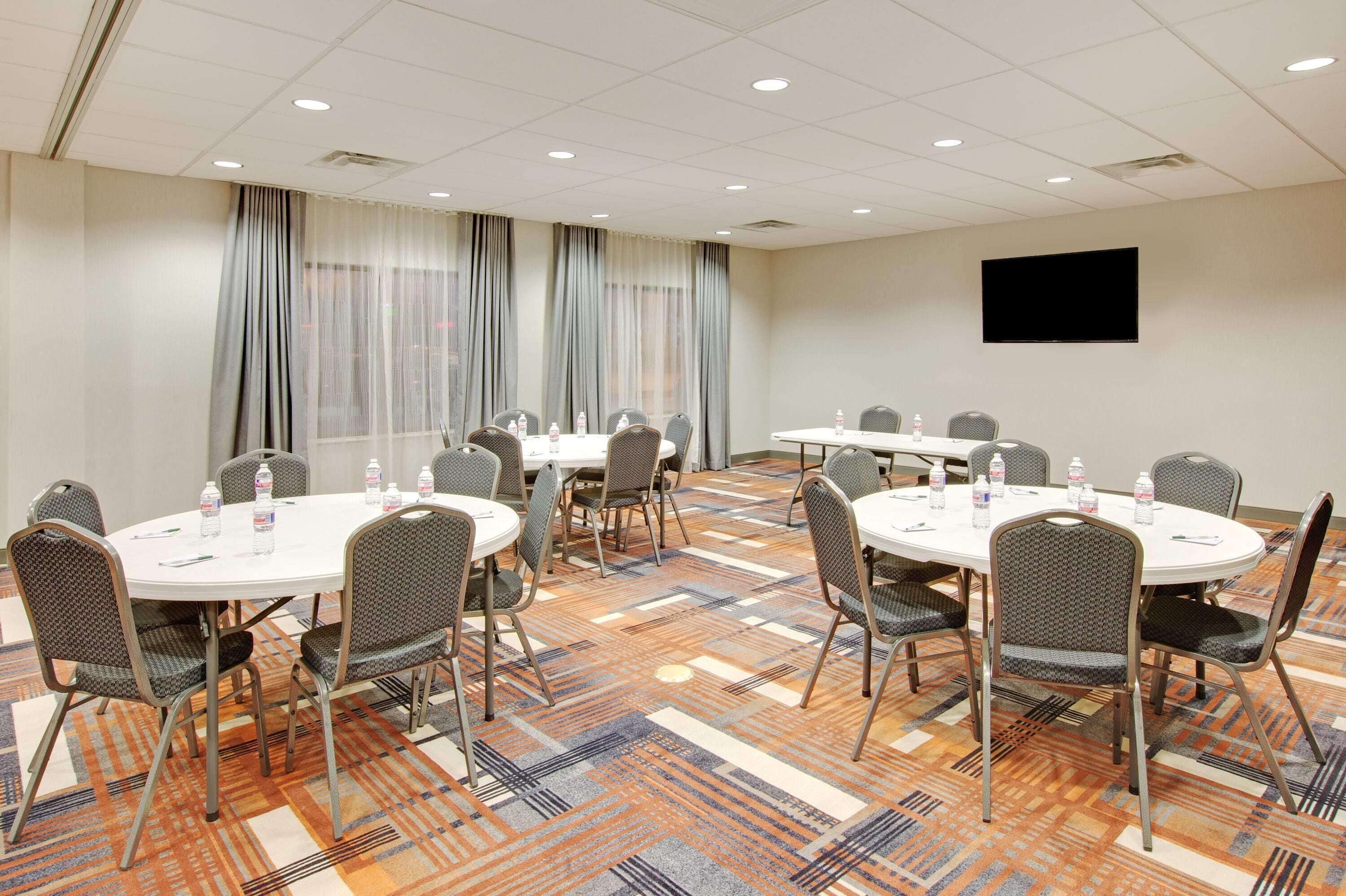 A conference room with round tables, chairs, and a flat-screen TV on the wall.