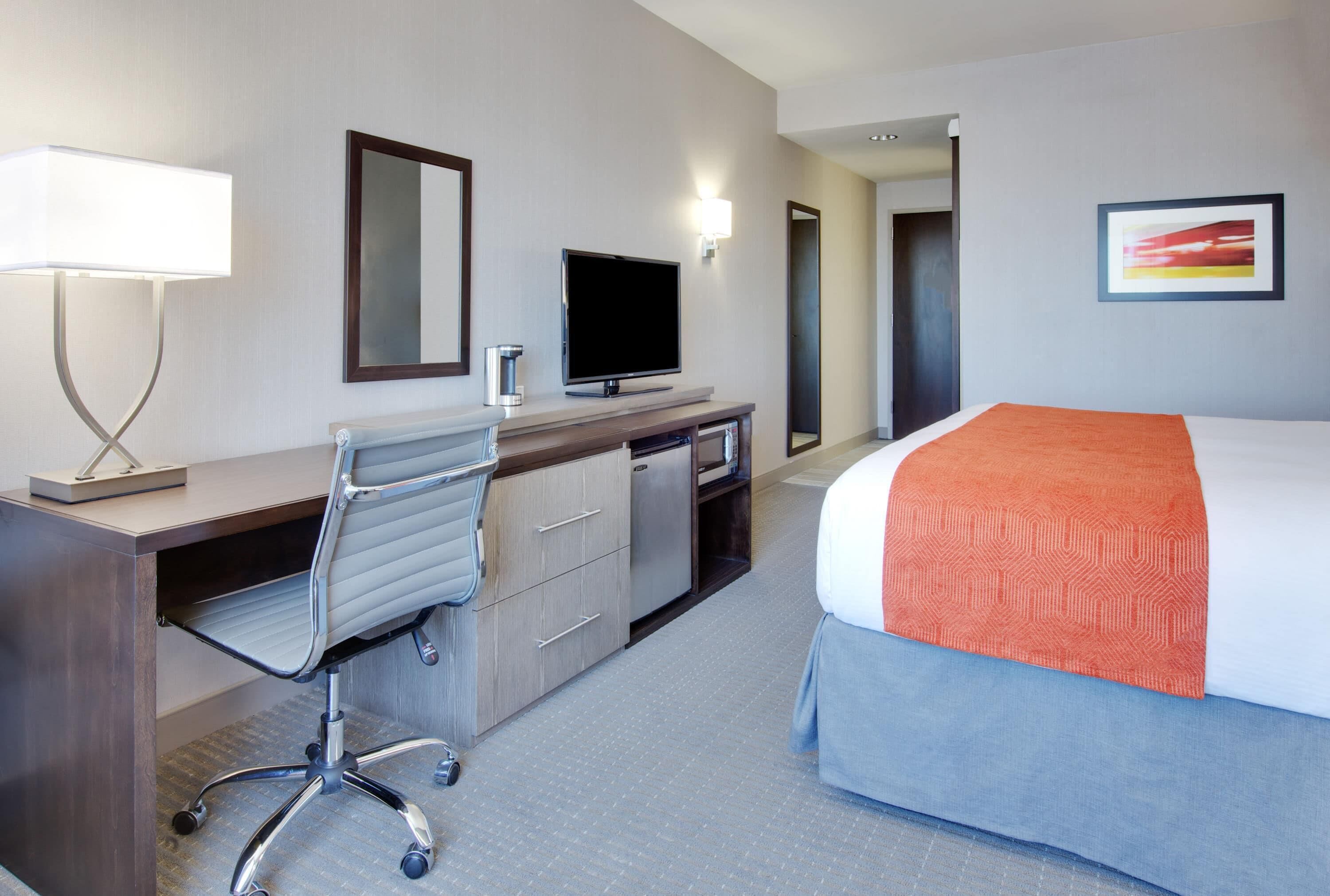 Une chambre d’hôtel avec un lit, un bureau, une chaise, une télévision et un tableau au mur.