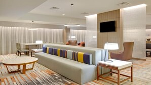 Una habitación de hotel moderna con sofá, una mesa redonda, televisor montado en la pared y alfombra estampada.