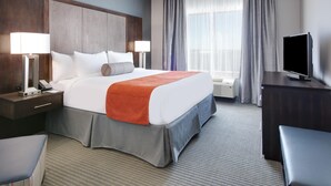Habitación de hotel con una cama grande, un escritorio con televisor, una silla, una lámpara y una ventana con cortinas.