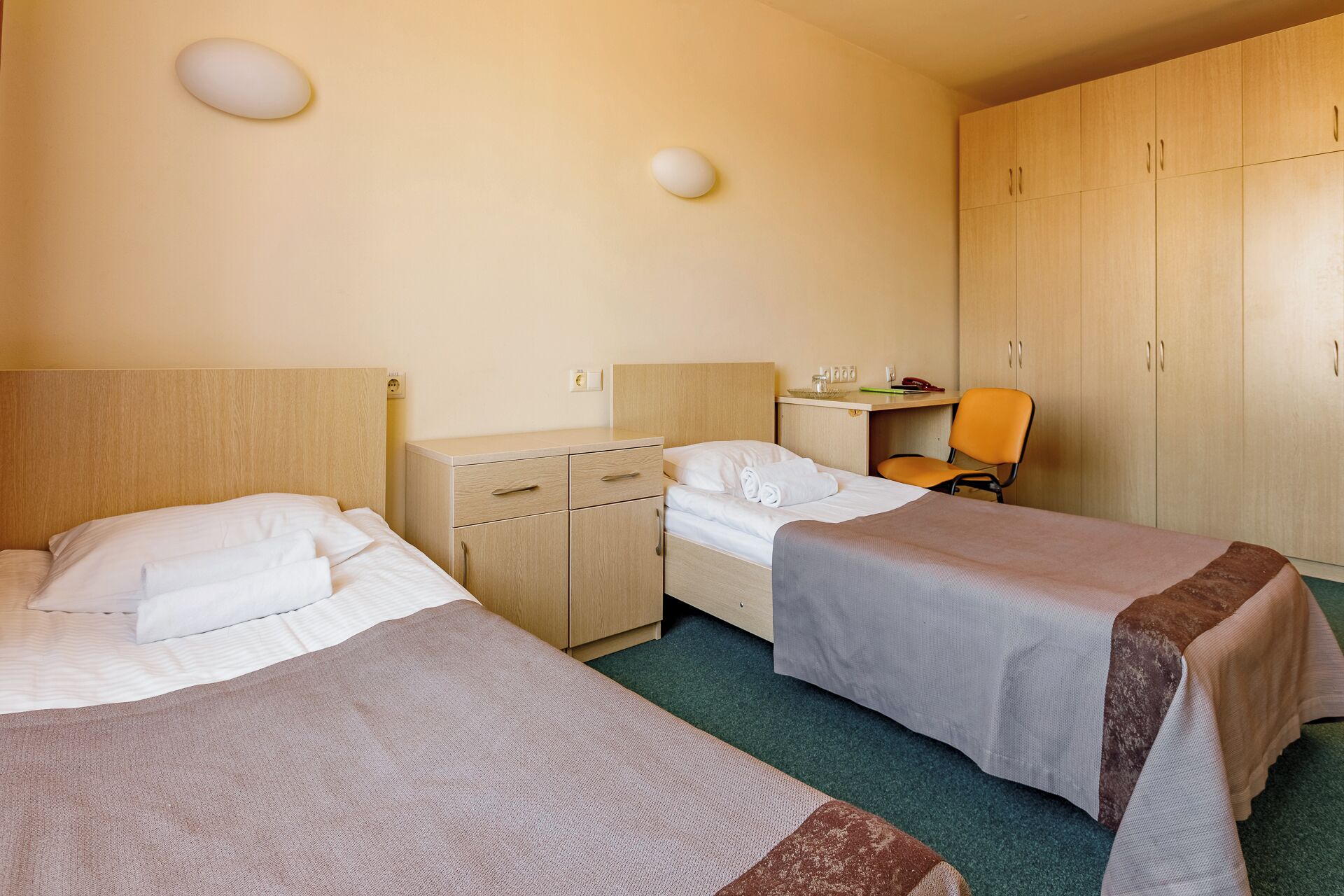 Een hotelkamer met twee enkele bedden, een bureau, een stoel en een kledingkast.