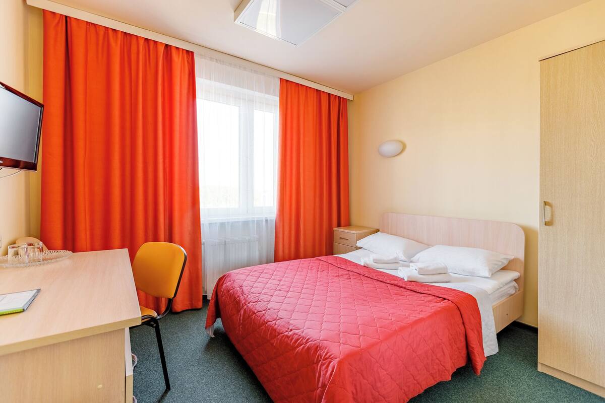 Habitación de hotel con cama, escritorio, silla, televisión y armario.