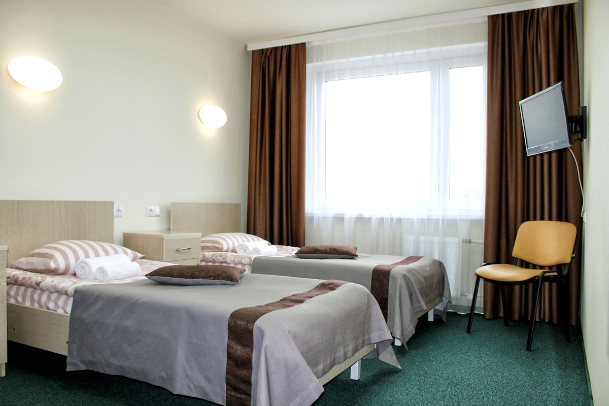 Habitación de hotel con dos camas, una silla, un televisor y una ventana con cortinas.