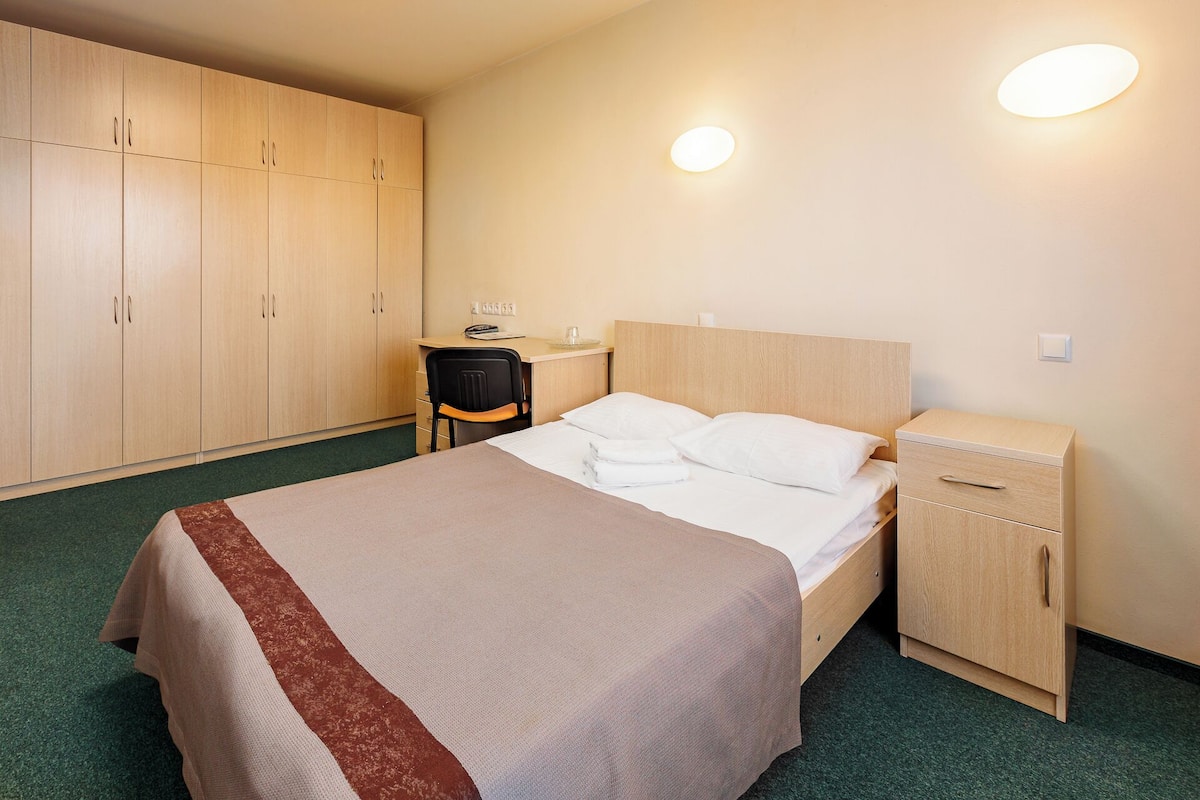 Habitación de hotel con cama, escritorio, silla, armario y dos luces fijadas a la pared.