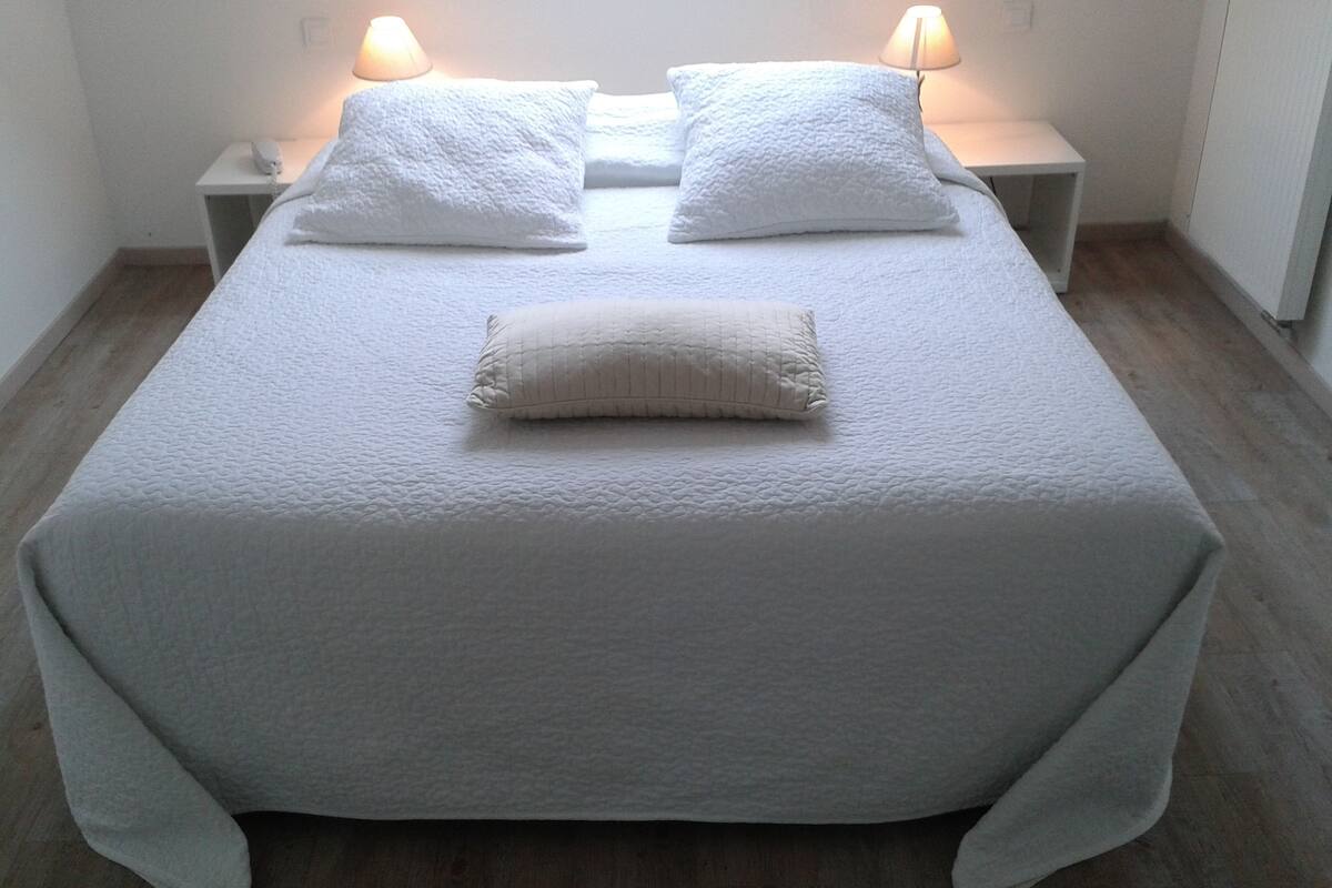 A neatly made bed with a white duvet and pillows, two bedside lamps, and a wooden floor.
