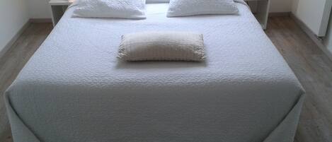 A neatly made bed with a white duvet and pillows, two bedside lamps, and a wooden floor.
