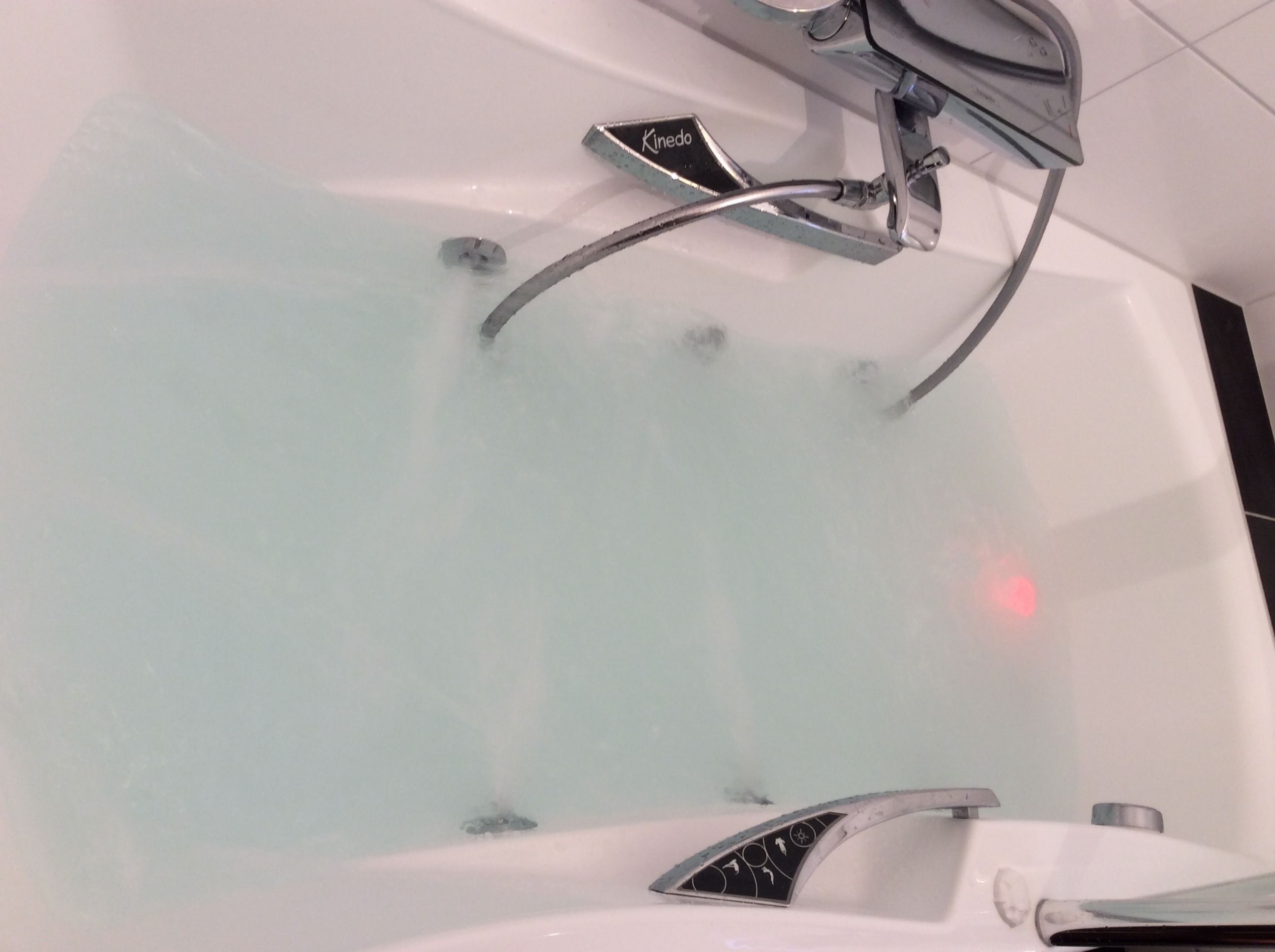 Eine Badewanne mit einem Chromarmaturen-Set und einer Bedieneinheit mit der Aufschrift 'Kinedo'.