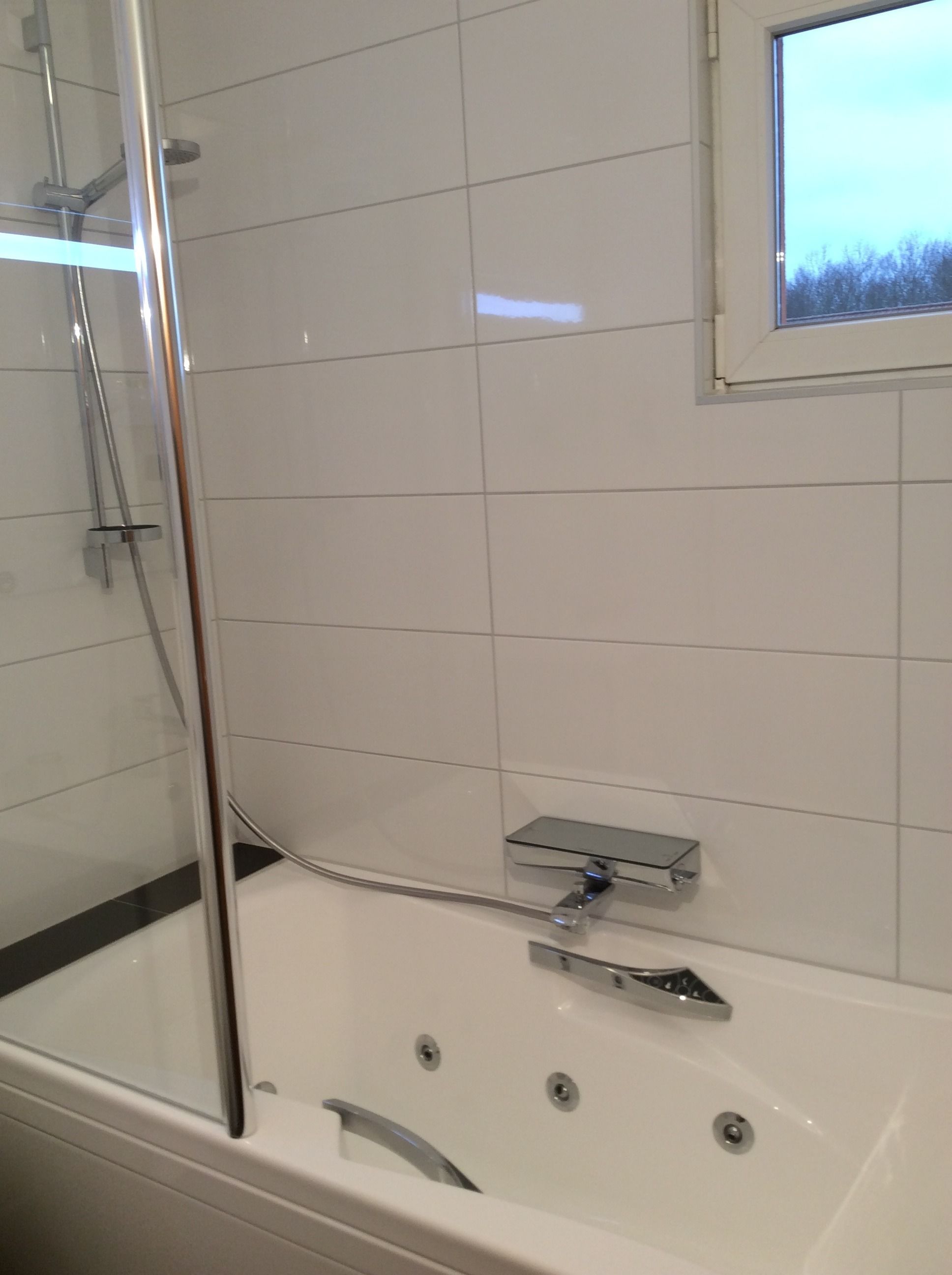 Ein modernes Badezimmer mit einer gläsernen Duschkabine, einer Badewanne mit chromfarbenen Wasserhahn und einer kleinen Ablagefläche.