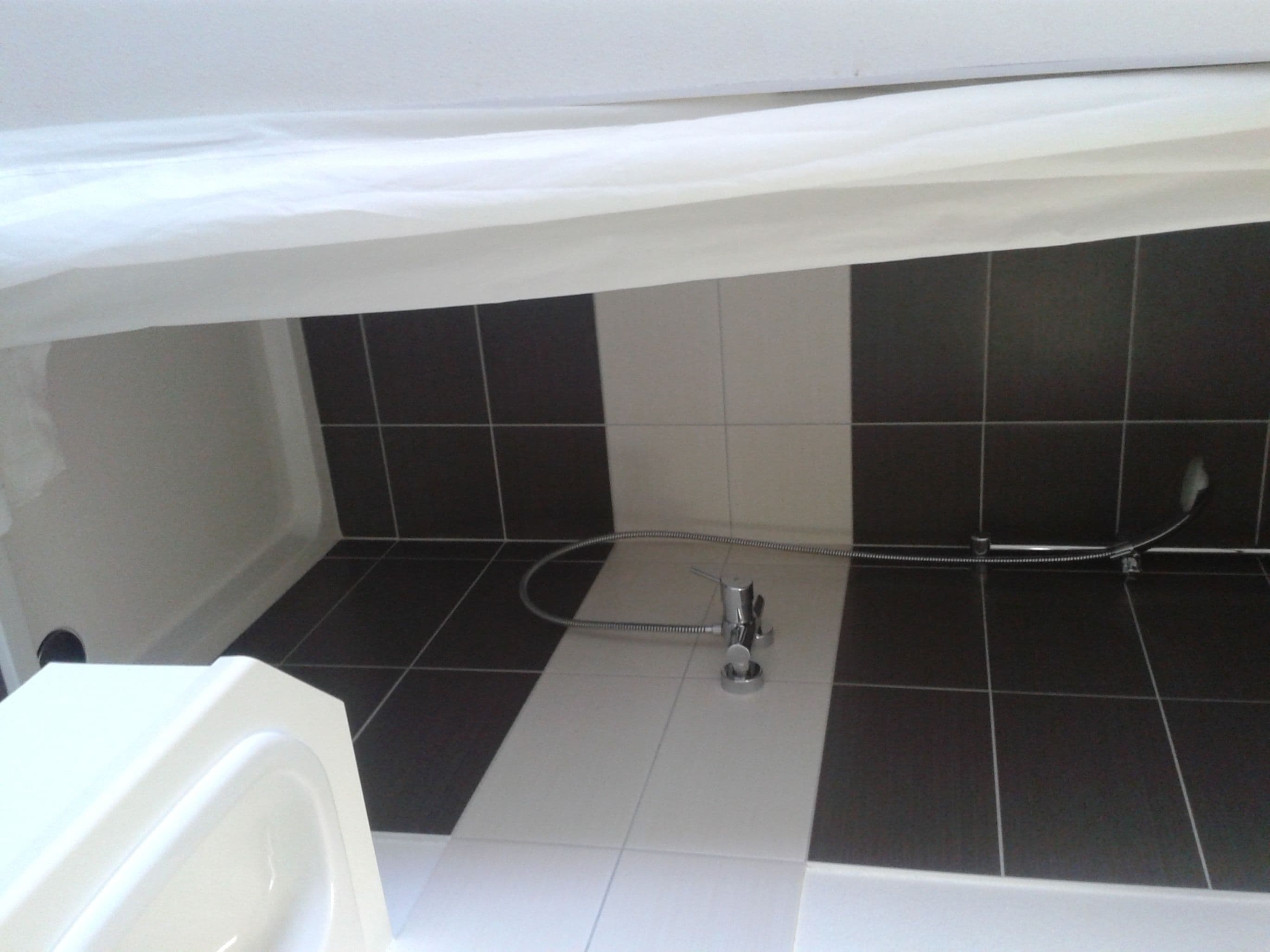 Une salle de bain avec des carreaux noirs et blancs, une baignoire et un espace douche.