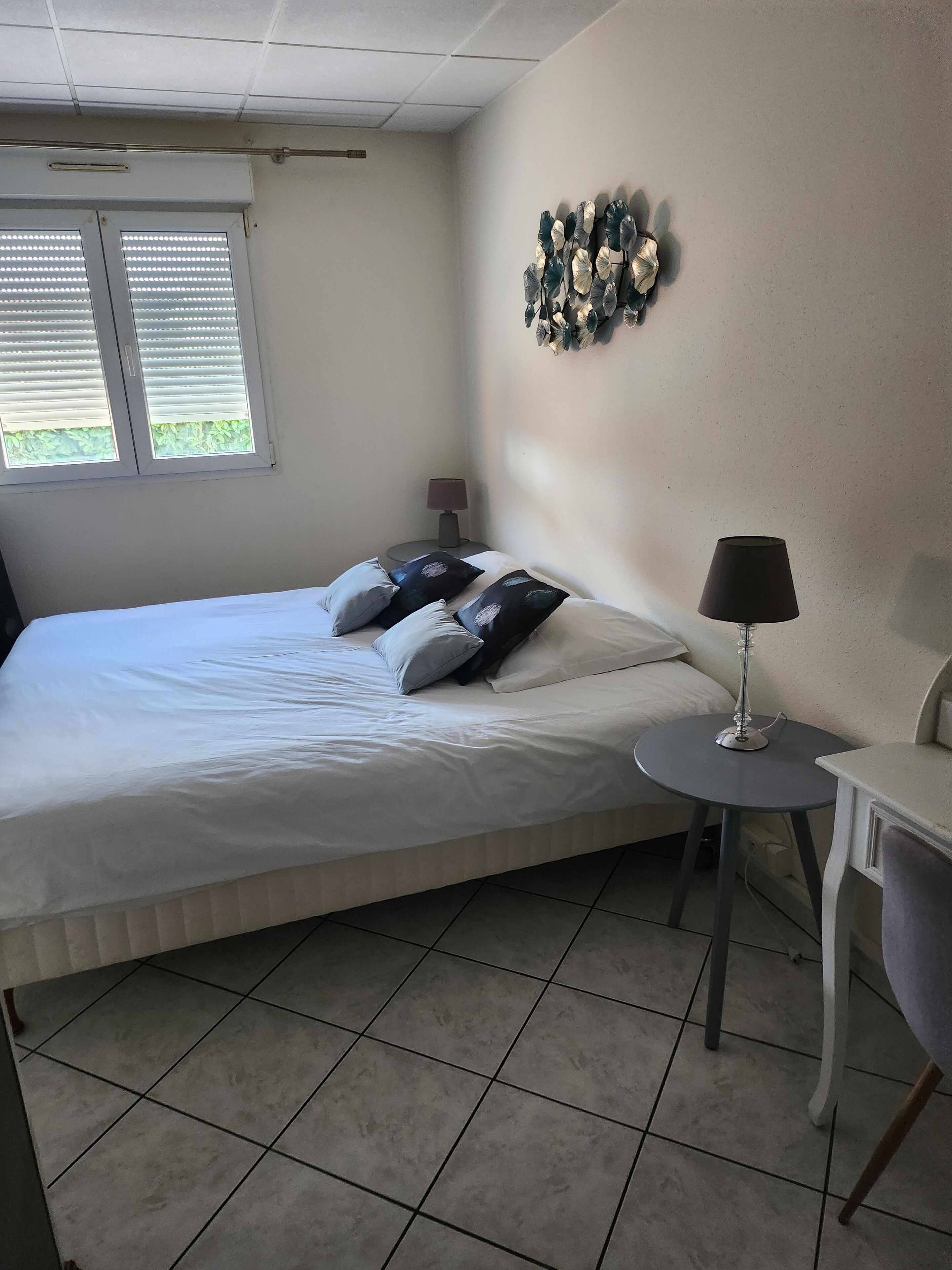 Un dormitorio con cama, mesita de noche, lámpara y un adorno en la pared.