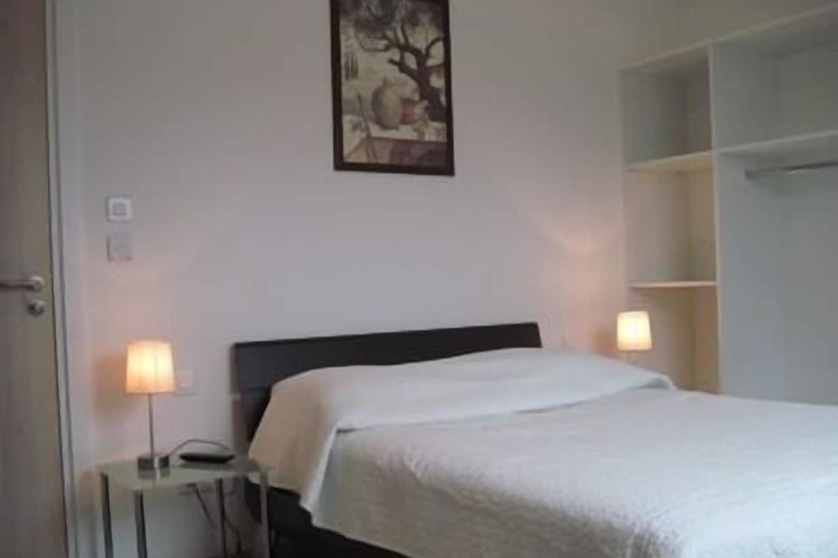 A bedroom with a bed, bedside lamps, a painting on the wall, and a door.