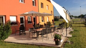An outdoor patio area with tables and chairs, a large umbrella, and potted plants. - Hotel des bois (Seltz)