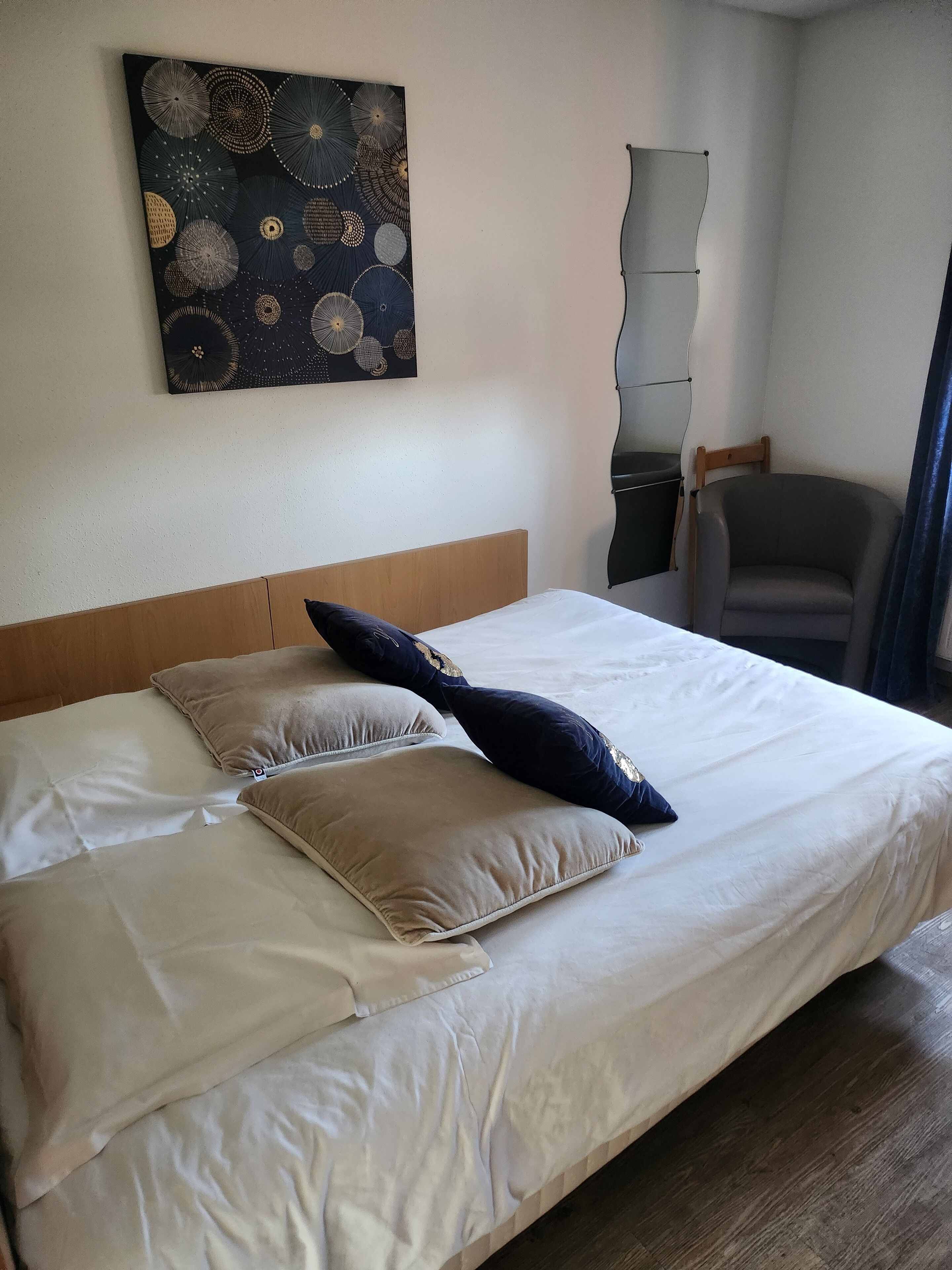 Una cama bien hecha con un cabecero de madera, almohada azul oscuro y almohadas color beige.
