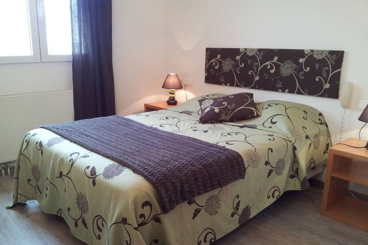 A neatly made bed with floral bedding, a bedside lamp, and a nightstand with a lamp.