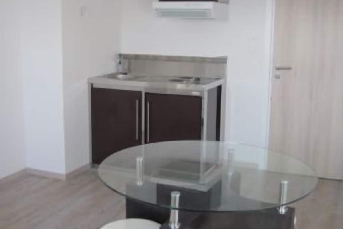 A modern kitchen with dark cabinets, a white countertop, and a built-in oven. There is a glass table with two black stools in front.